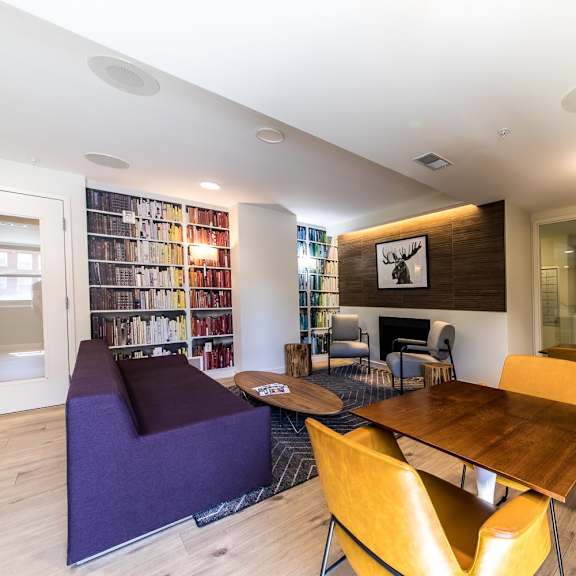 a room with a wooden table and chairs, a purple bench, and a bookshelf filled with books.
