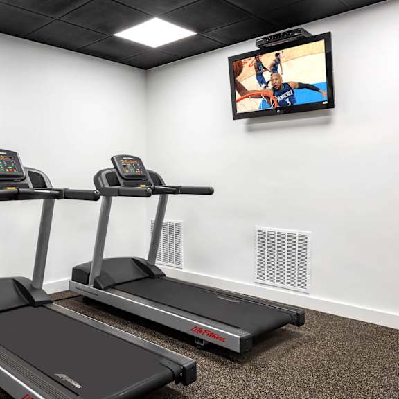 two treadmills are in a room with a television mounted on the wall.