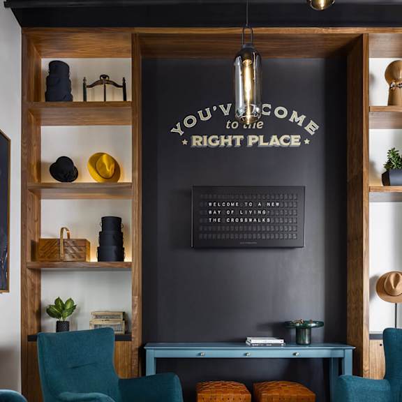 a living room with a grey wall and a wooden shelf with a sign that says "you're welcome to my right place".