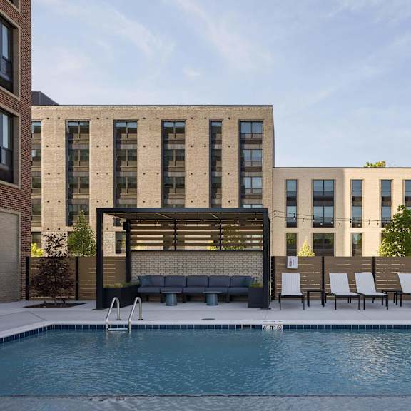 a pool in front of a building with a bench and chairs.