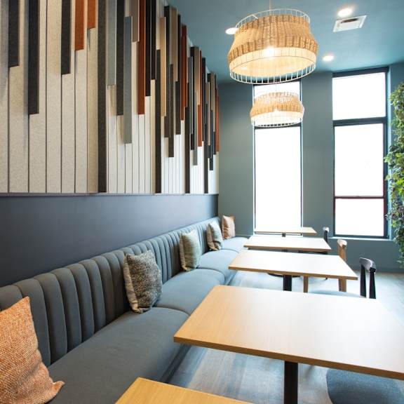 a long wooden table is in the middle of a room with a grey couch and a wall with wooden slats.