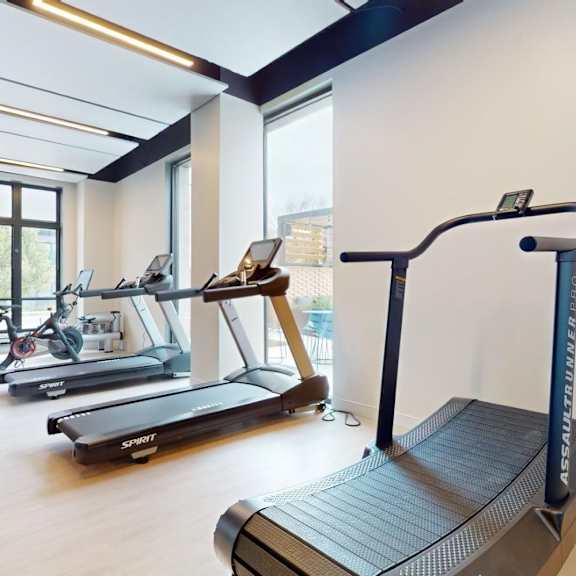 a treadmill with the brand name assault unlimited is in the foreground of a gym with other treadmills and exercise equipment.