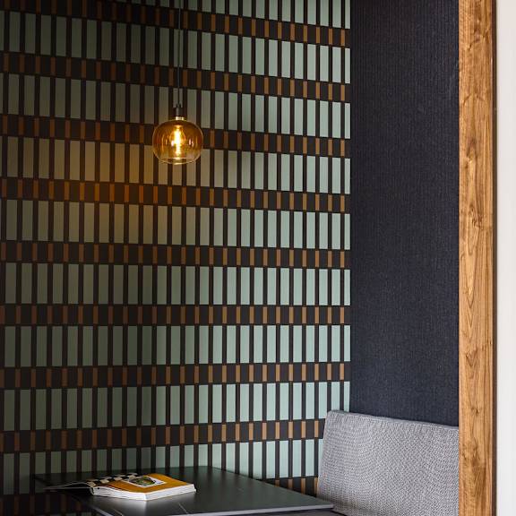 a small table with a book on it and a grey cushioned bench in front of a wall with a wooden frame.