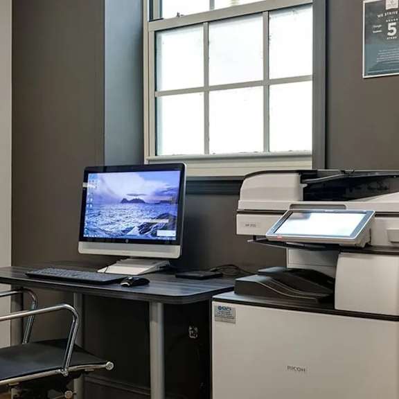 a black chair is in front of a desk with a monitor, keyboard, and a printer.
