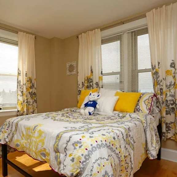 a bedroom with a bed in the center and floral curtains on the windows.