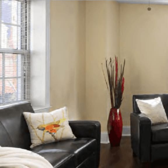 a living room with a black couch, a dining table with chairs, and a vase with flowers on the table.