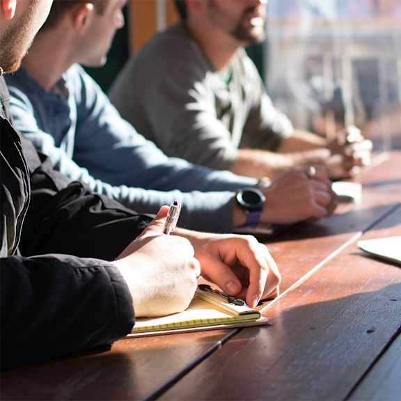 three people are sitting at a table writing in notebooks.