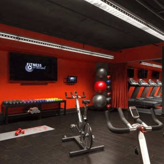 a gym with a red wall and black flooring has a variety of exercise equipment.