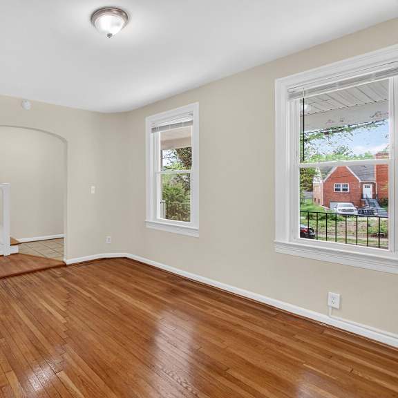 a room with wooden floors and a window showing a red house outside.