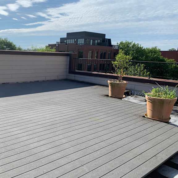 a rooftop with grey wooden planks and two potted plants.