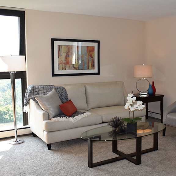 a living room with a white couch, a grey armchair, a glass coffee table, and a framed picture on the wall.