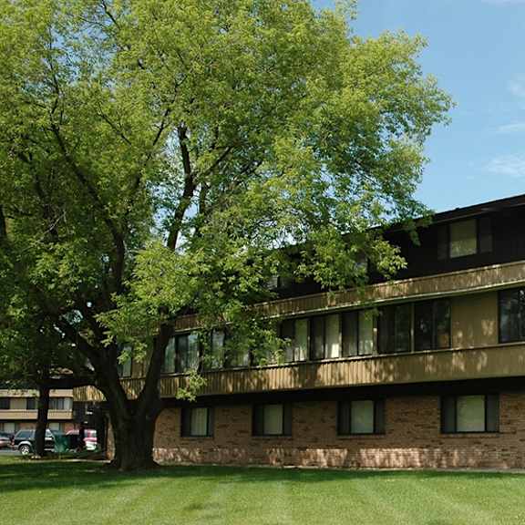 a large brown building with a balcony on the second floor is surrounded by trees.