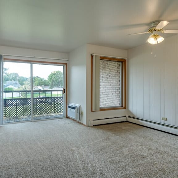a room with a carpeted floor, a ceiling fan, and a sliding glass door leading to a balcony.