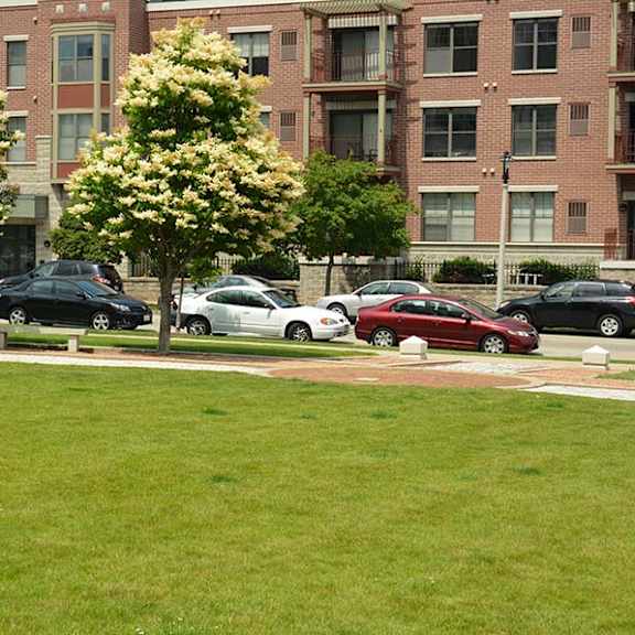 a grassy area in front of apartment buildings with cars parked in the background.