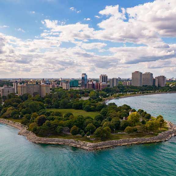 a small island with a forest in the middle of a large body of water with a city in the background.