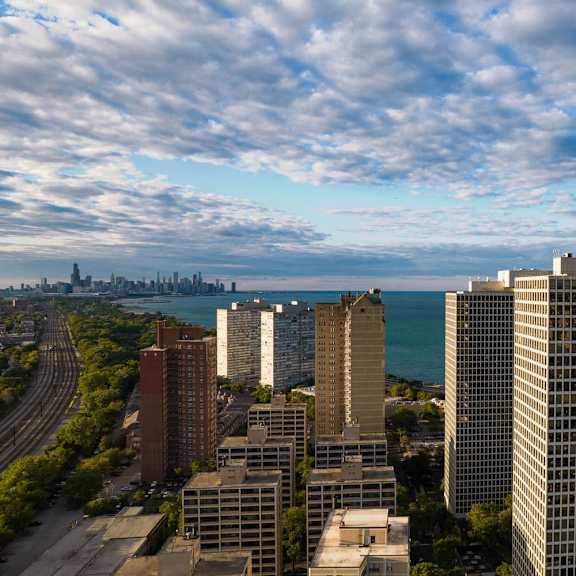 a cityscape with a mix of modern and older buildings, a highway, and a body of water in the distance.
