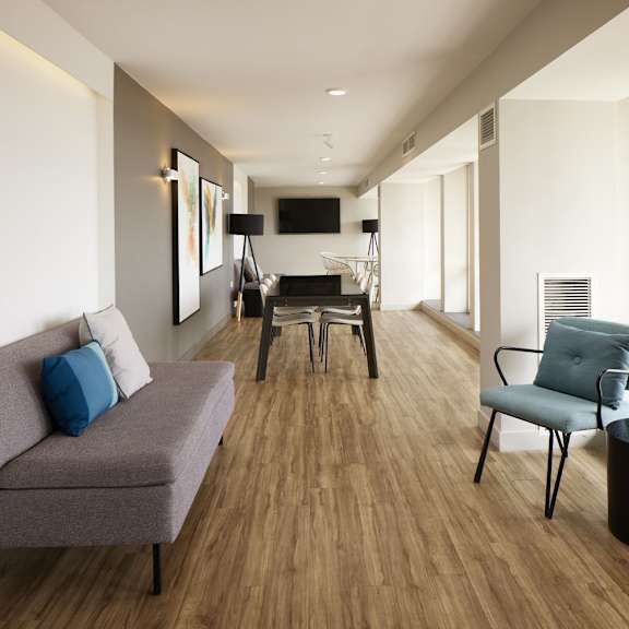a grey couch with a blue pillow sits in a room with wooden floors and white walls.