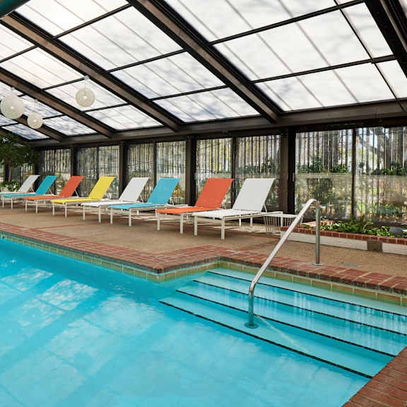 a large indoor swimming pool with a glass ceiling and colorful lounge chairs.