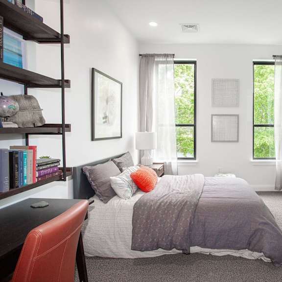 a bedroom with a bed, nightstand, chair, and window.