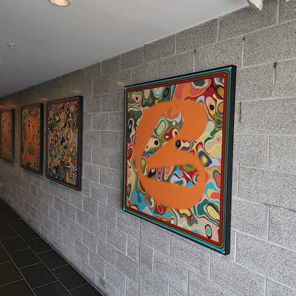 a wall with a large orange painting and three smaller paintings behind it.