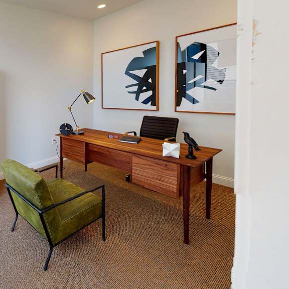 a room with a desk, chair, and two pictures on the wall.