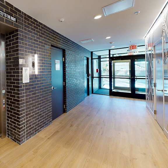 a hallway with a brick wall and a wooden floor leading to a glass door.