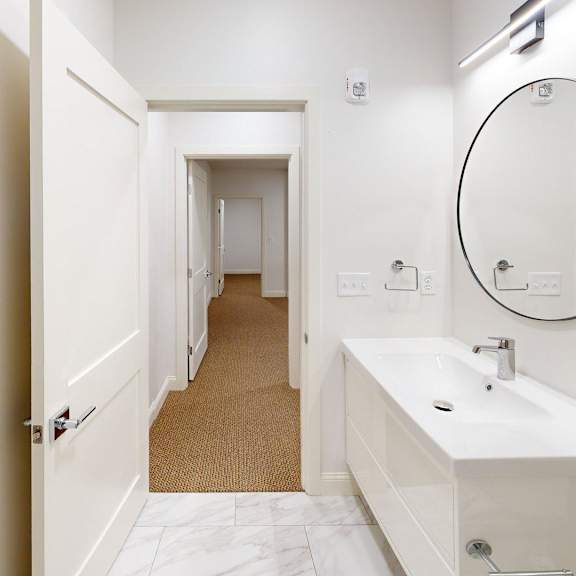 a white bathroom with a round mirror and a white sink.