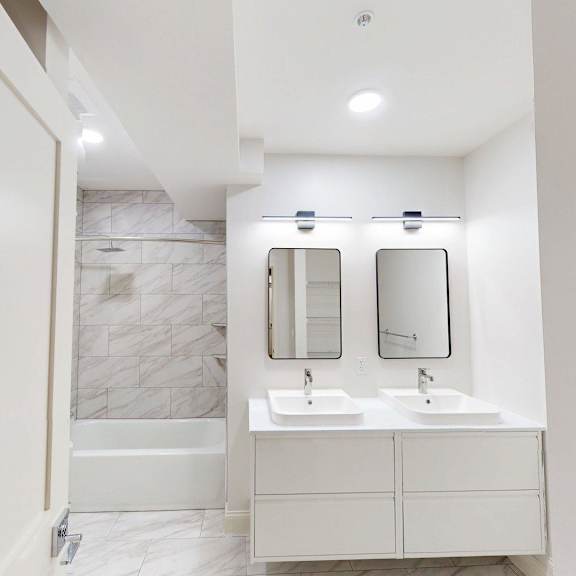 a white bathroom with a marble tile shower and a double sink vanity.