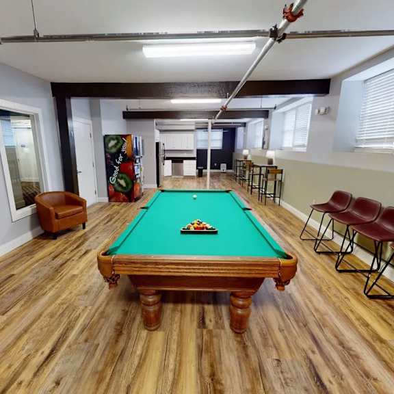 a pool table in a room with wooden flooring and chairs.
