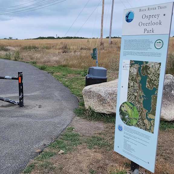 a sign for the back river trail stands next to a paved path.