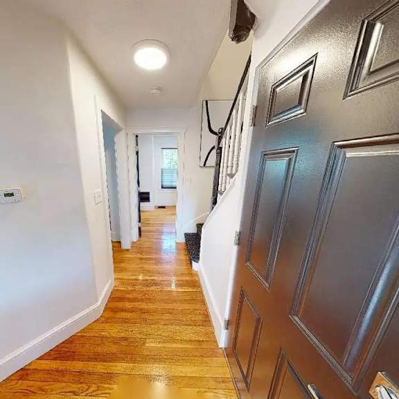 a hallway with wooden floors and a white wall on the left.