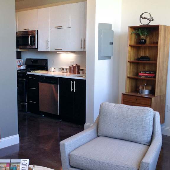 a grey chair is in the foreground of a kitchen.