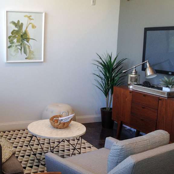 a living room with a brown couch, a white ottoman, and a painting on the wall.