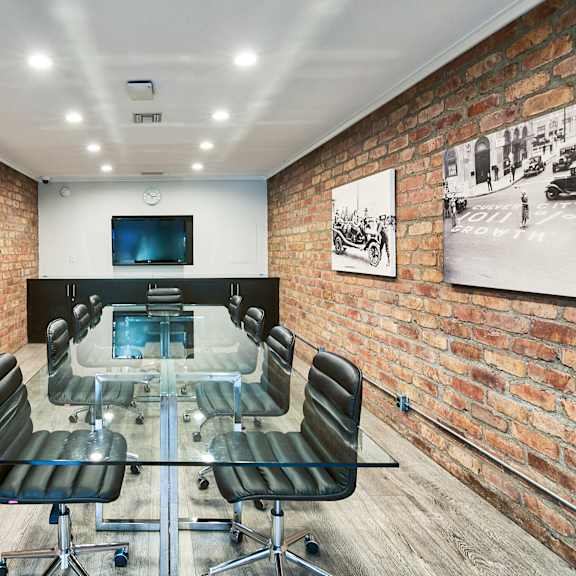 a conference room with a glass table and chairs, a television, and framed pictures on the brick walls at the meadows apartments, culver city , ca 90230