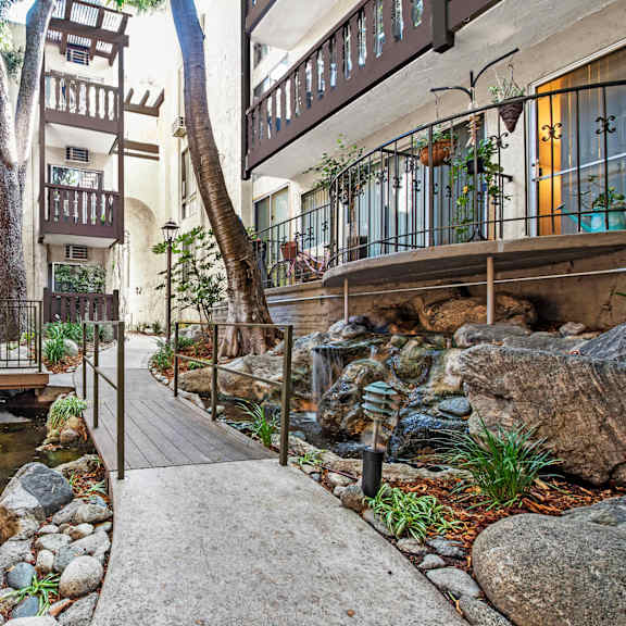 a small pond with rocks and a wooden walkway in the middle of a courtyard at mediterranean village west hollywood, west hollywood, 90069