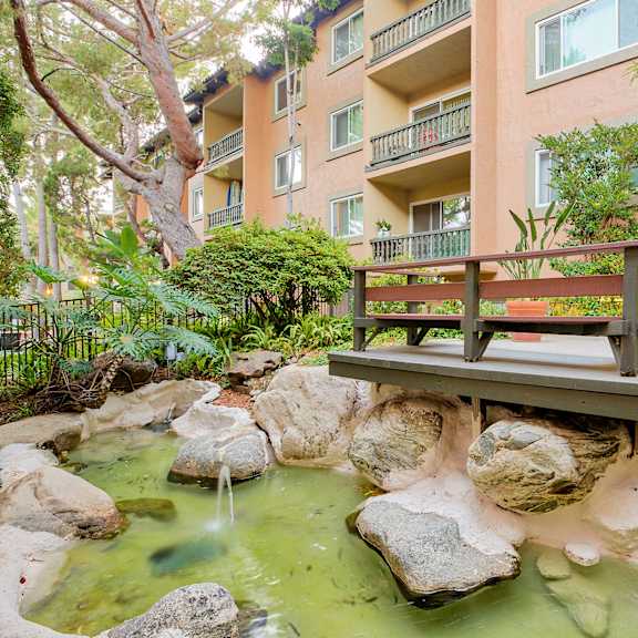 a bench sits on a bridge over a stream in front of an apartment building at casa granada, los angeles, ca