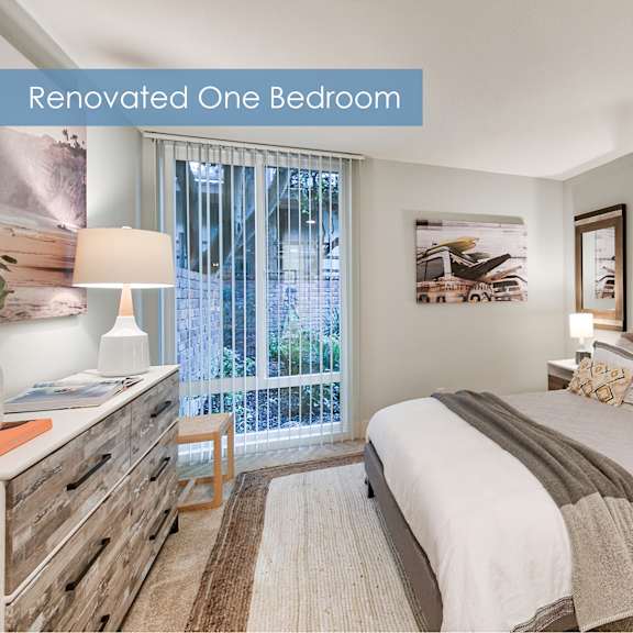 a renovated bedroom with a large bed, a nightstand, and a window with a view at the meadows apartments, culver city , ca 90230