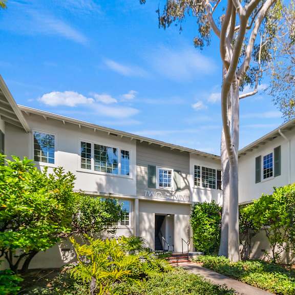 a white two-story house with a tree in front at sunset barrington gardens, los angeles, 90049