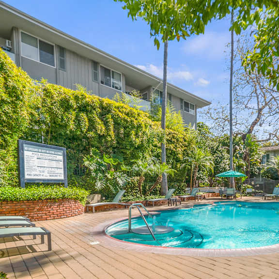 a pool surrounded by a wooden deck and green trees at sunset barrington gardens, los angeles, 90049