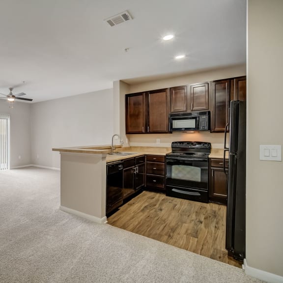 Thumbnail 4 of 5 an empty living room with a kitchen with a stove and refrigerator at Las Brisas Apartment Homes, Round Rock