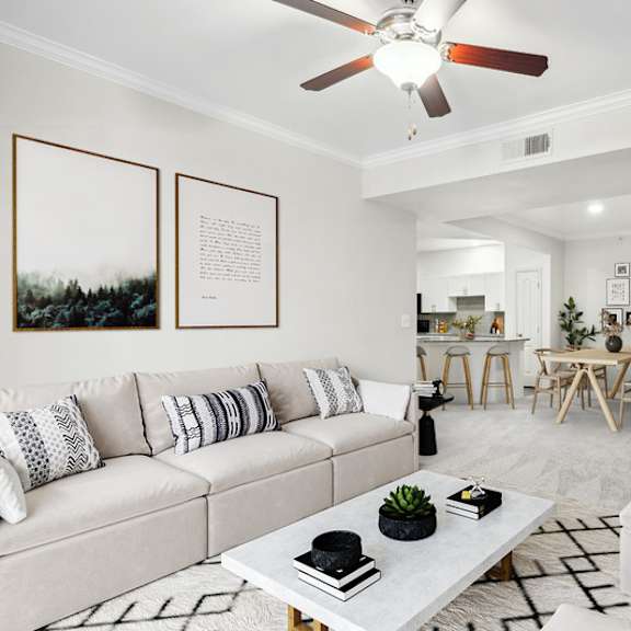 Thumbnail 5 of 16 A living room with a white couch, a coffee table, and a ceiling fan.