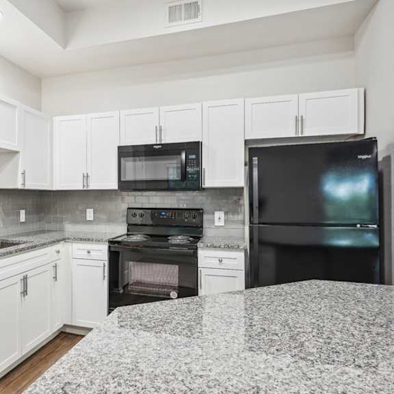 Thumbnail 7 of 16 A kitchen with black appliances and white cabinets.