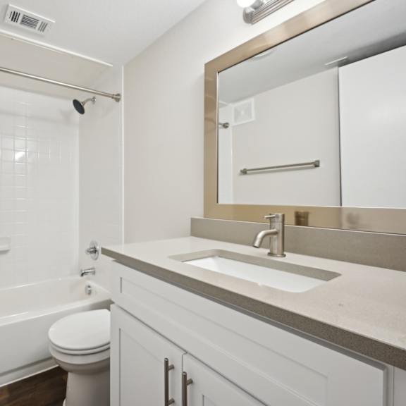 a bathroom with bright lights and white cabinets at woodlands of plano in plano, tx