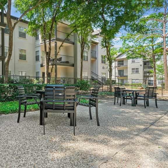 an al fresco dining patio with a table and chairs surrounded by lush trees at jefferson place apartments in irving, tx