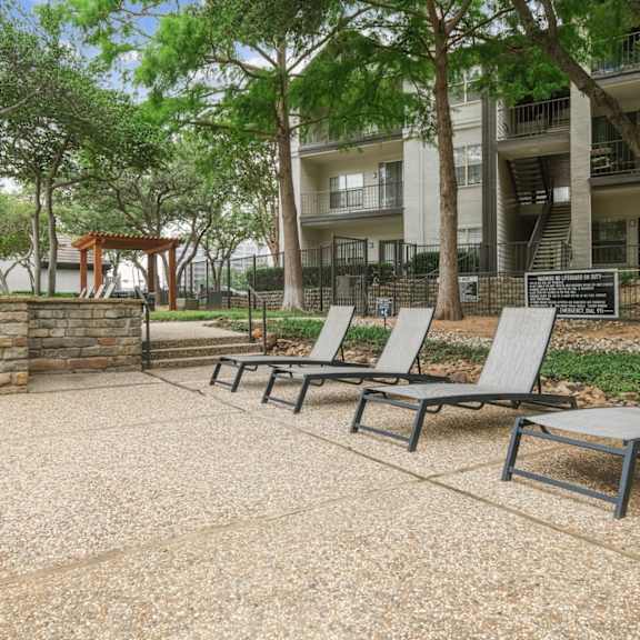 pool loungers in the pool area with apartment buildings in the background at jefferson place apartments in irving, tx