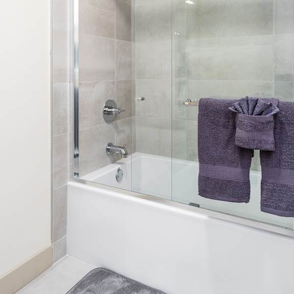 bathtub with glass shower doors and purple towels at lido - 1532 brockton ave apartments, los angeles, ca 90025