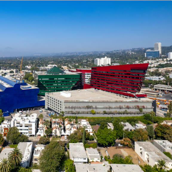 a large building with a red and green section is in the foreground of a cityscape.