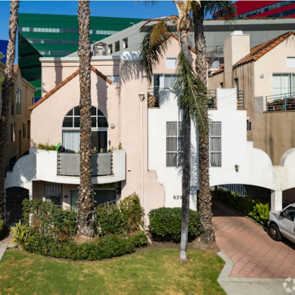 a white building with a balcony is surrounded by greenery.