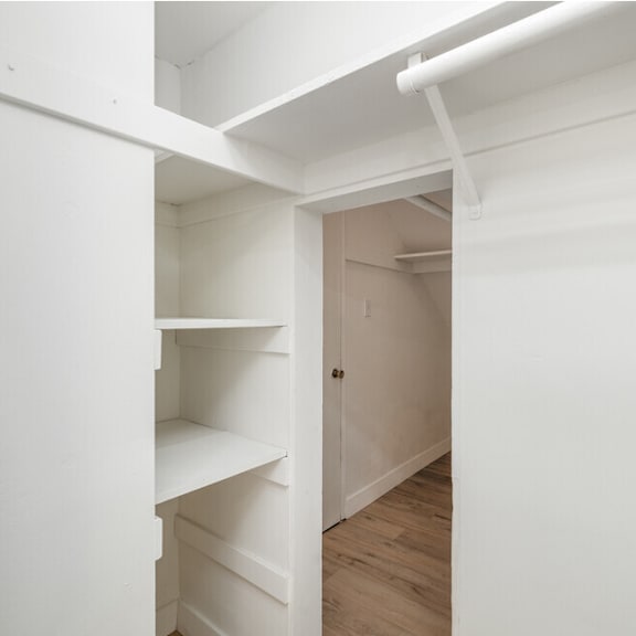 a walk in closet with white walls and shelves and a door