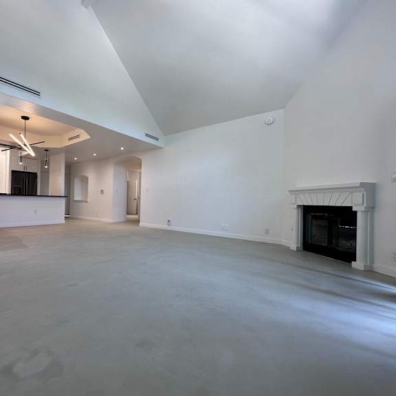 a large, empty room with a fireplace and a kitchen area in the background.